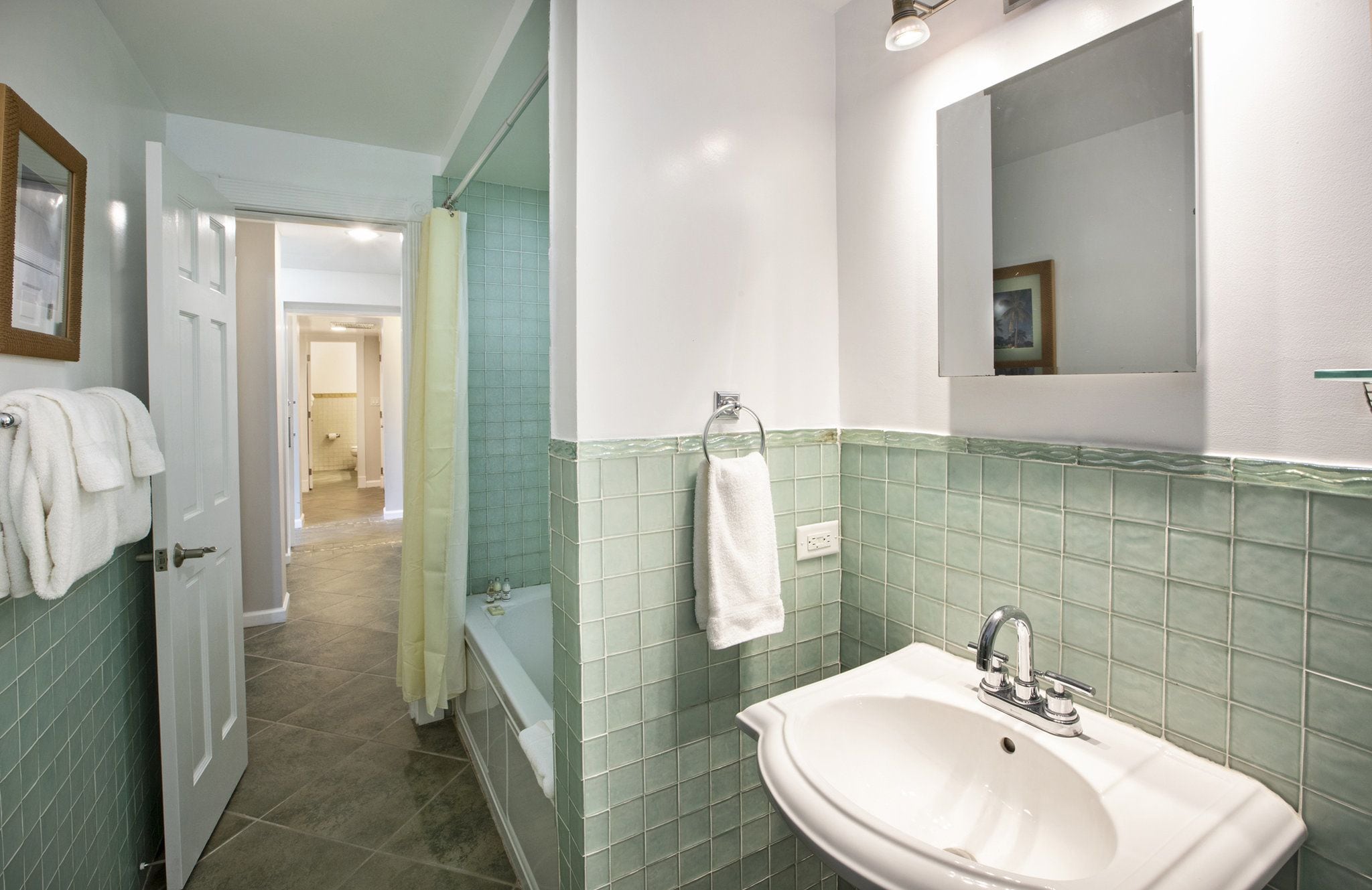 A bathroom with a sink, mirror, and green-tiled walls. A door leads to another room.