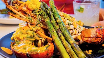Ein Teller mit Meeresfrüchten und Gemüse, darunter Hummer, Spargel und eine Tomate, serviert auf einem dunklen Teller.