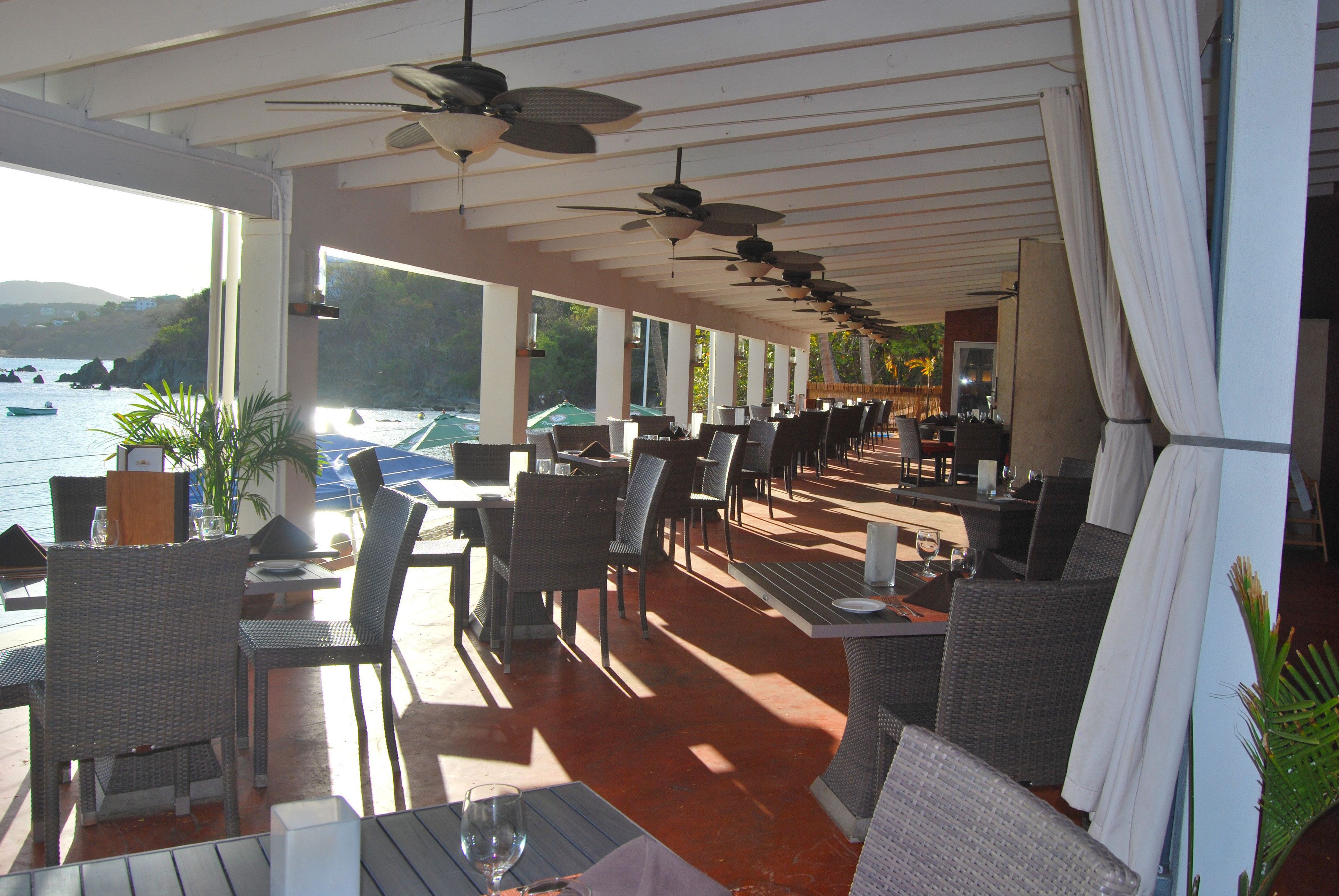 An outdoor dining area with wicker furniture, ceiling fans, and a view of the sea.