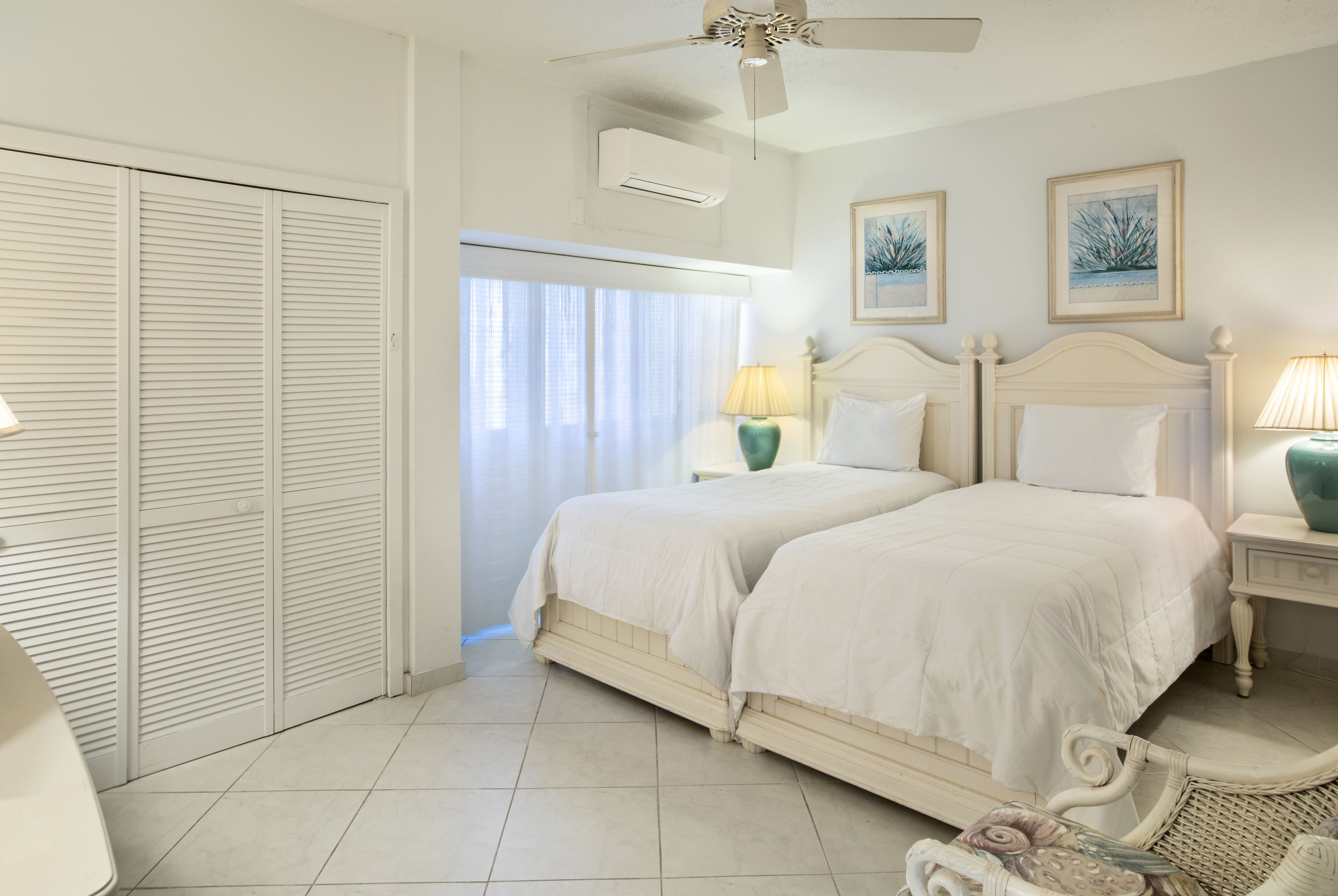 A bedroom with two beds, a ceiling fan, and a view of the outdoors through a window.