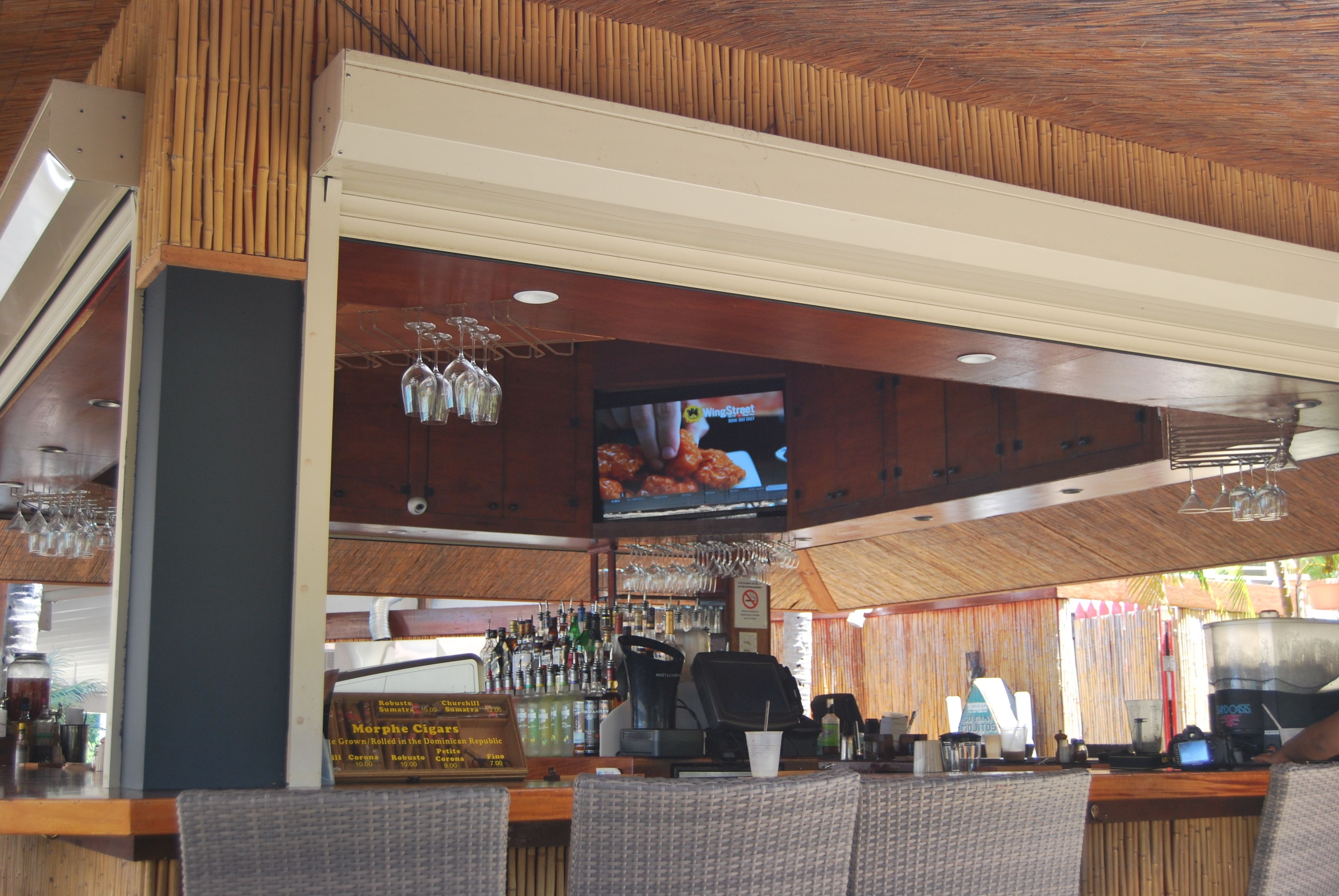 A bar area with a television displaying a food program, a cash register, and various bar items.