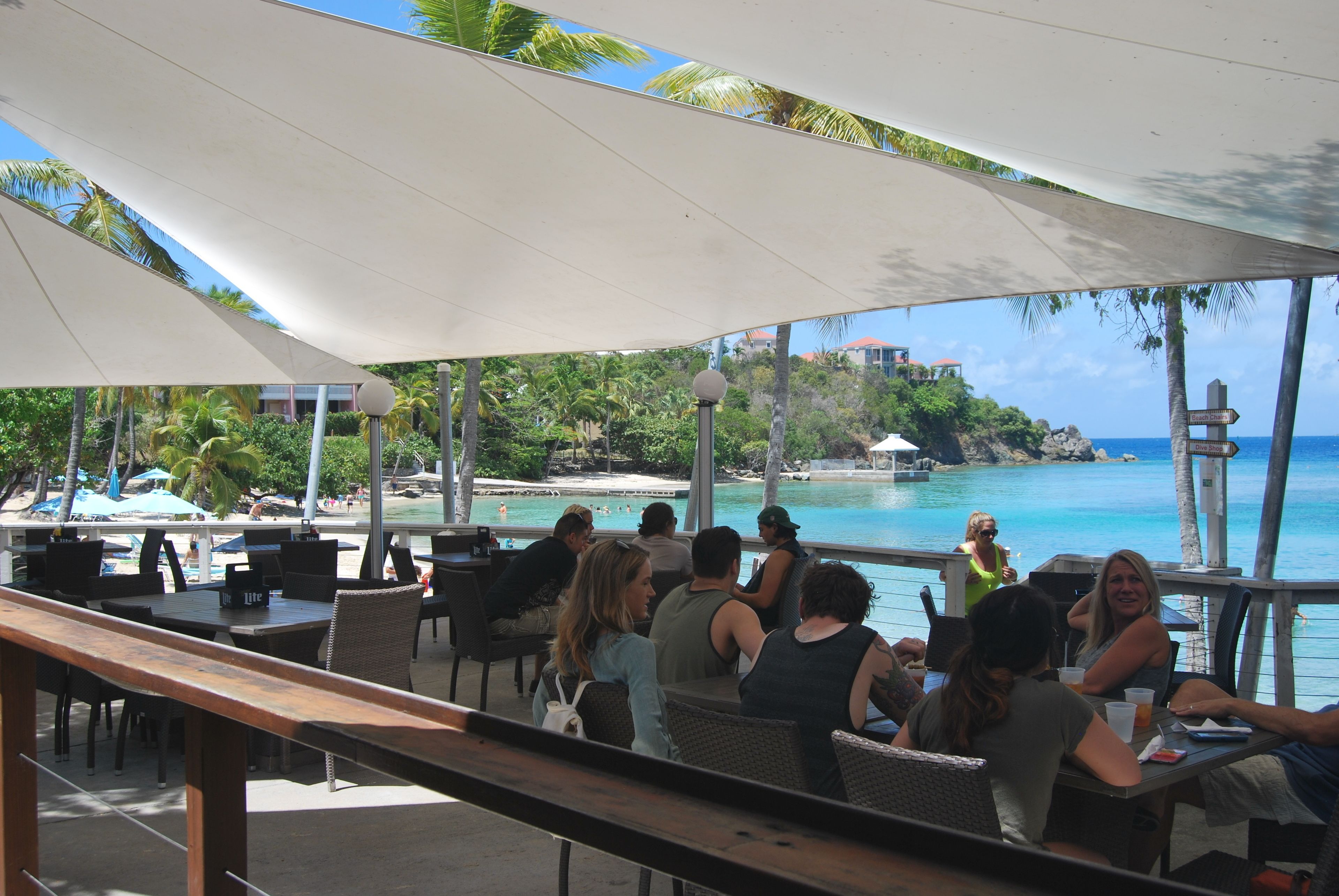 Un espace extérieur aménagé pour les repas, avec des tables et des chaises, offrant une vue sur une plage et l’océan.