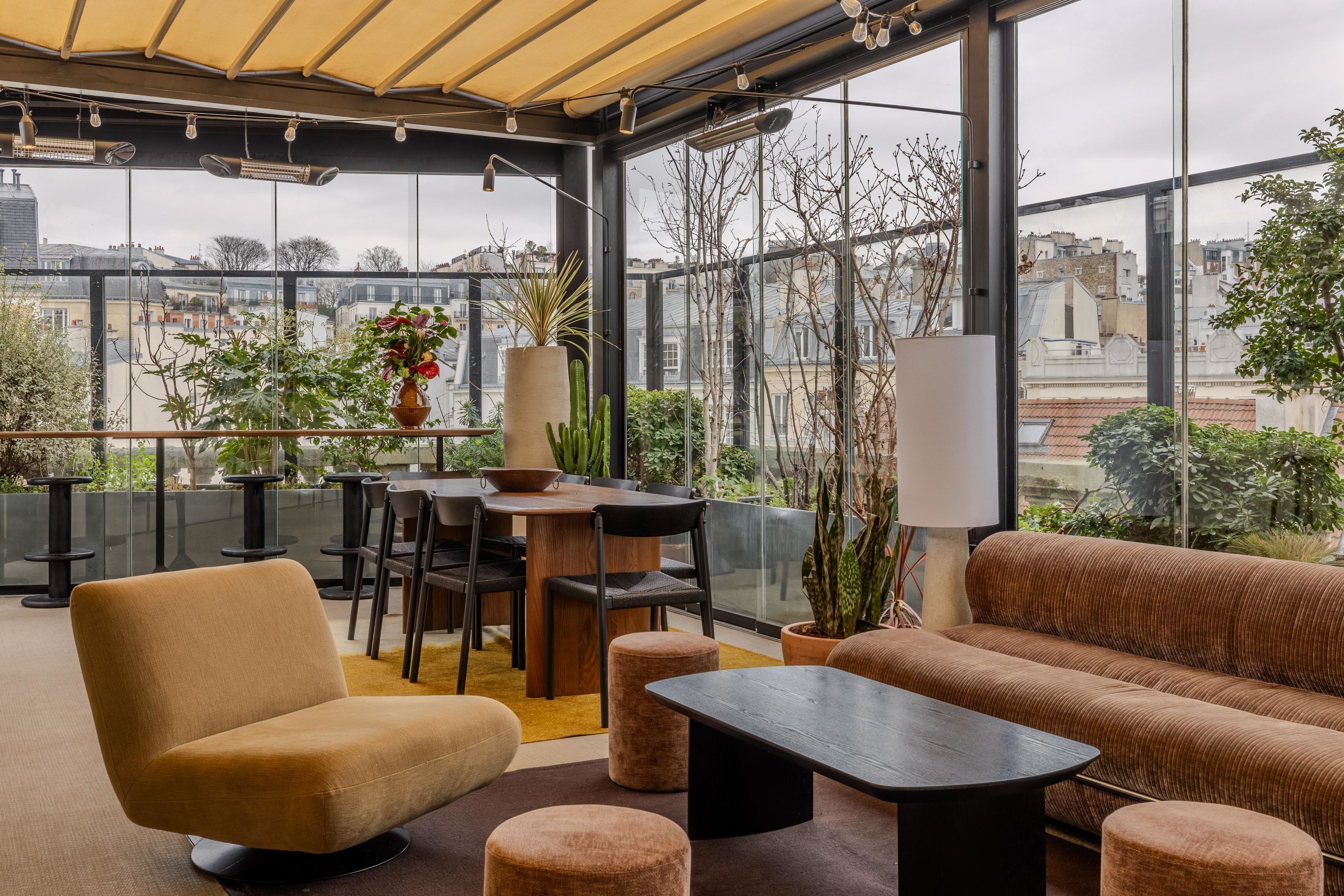 A modern outdoor seating area with a sofa, chairs, and a table, surrounded by large windows offering city views.