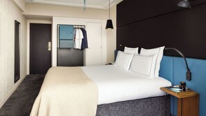 Una habitación de hotel con una cama grande, una mesita de noche con lámpara, un espejo y un armario.