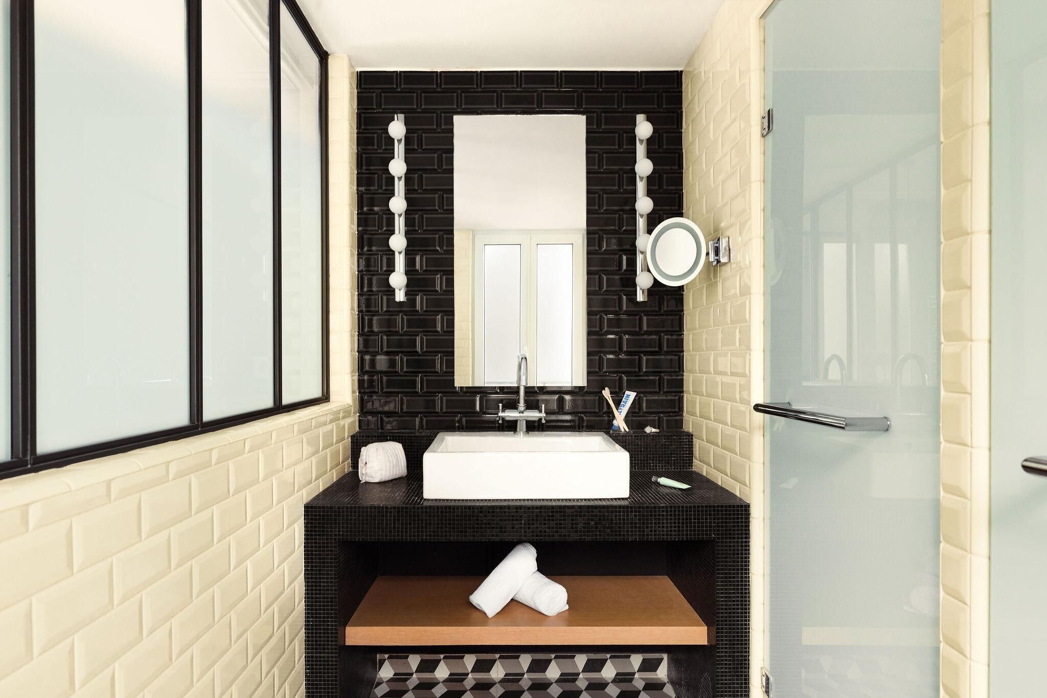 Un baño moderno con salpicadero de azulejos blancos y negros, un espejo grande, un lavabo blanco y una cabina de ducha con mampara de vidrio.
