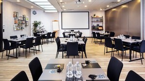 Un salón de conferencias con varias mesas, sillas, una pantalla de proyector y una pizarra.