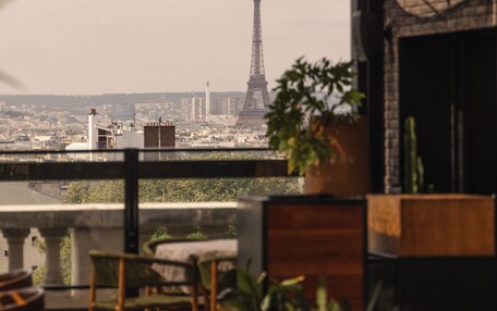 A rooftop terrace with a view of the Eiffel Tower, outdoor seating, and potted plants.
