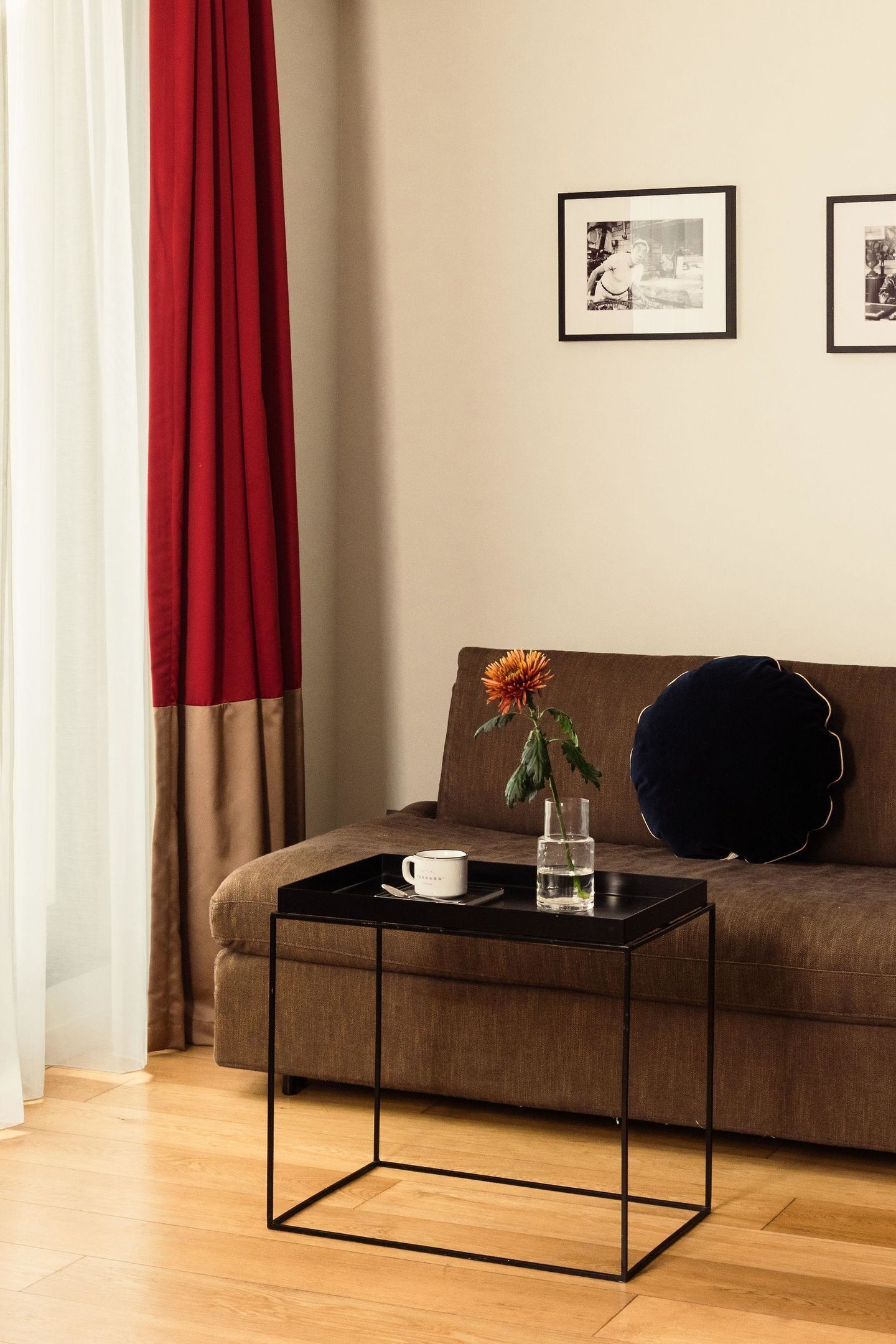 Una sala de estar moderna con un sofá marrón, una mesa de centro negra y un florero con una flor. Hay dos cuadros en la pared.