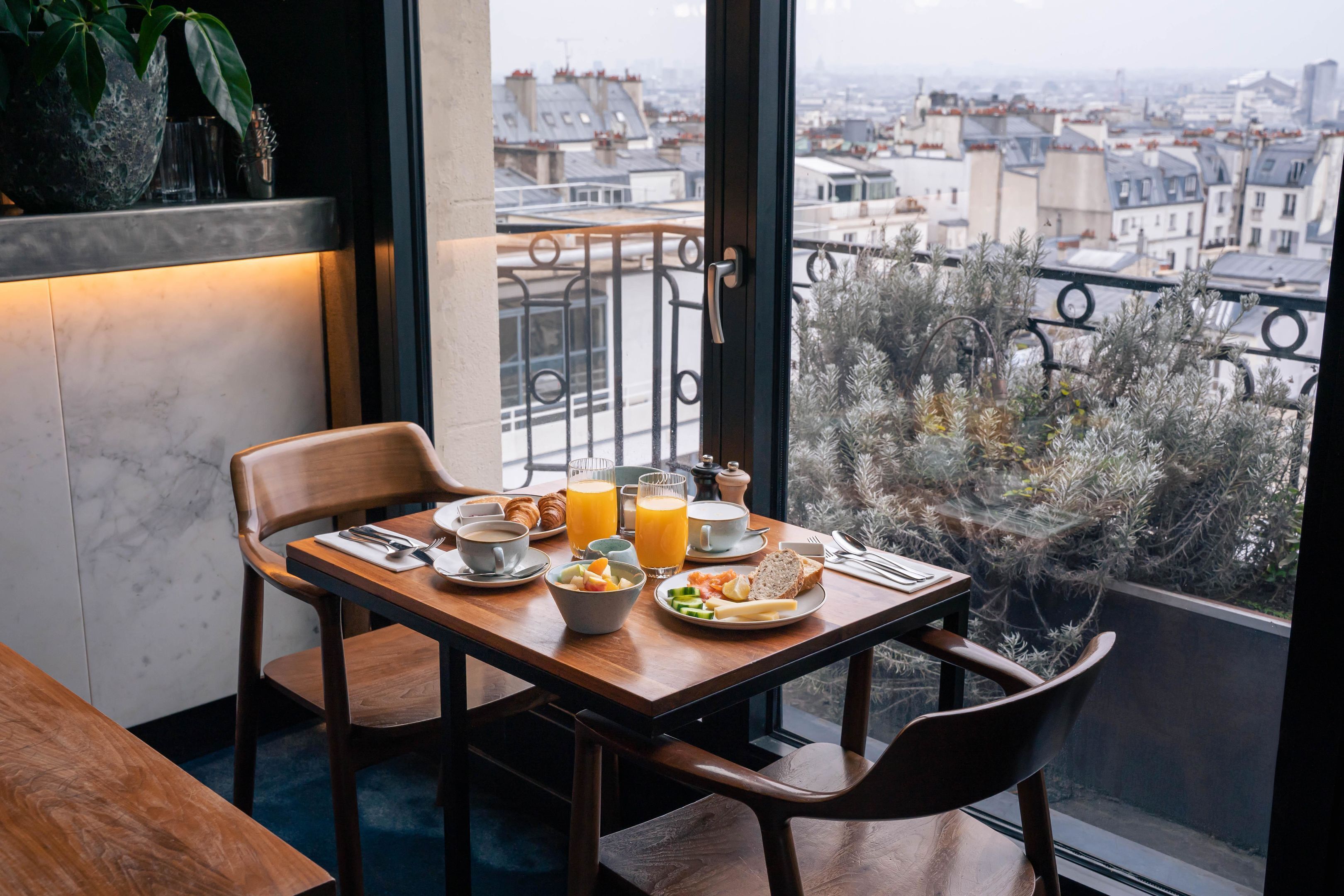 A dining table set with breakfast items, a view of a cityscape through a balcony railing.