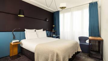 Una habitación de hotel con una cama grande, mesitas de noche, una silla y un escritorio.