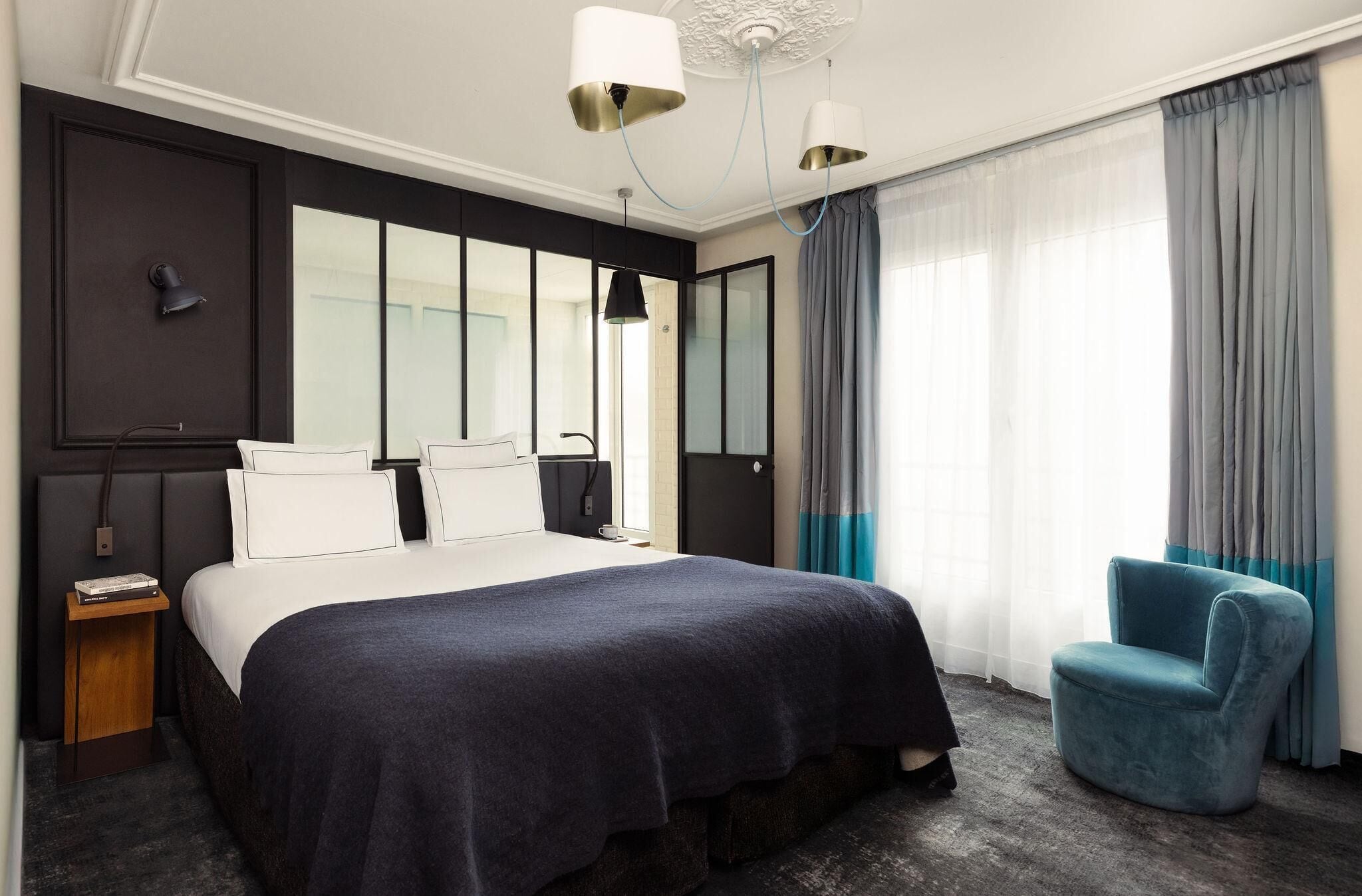 Une chambre d’hôtel moderne avec un grand lit, une table de chevet, une chaise et une grande fenêtre avec des rideaux.