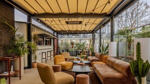 Un área lounge moderna al aire libre con asientos cómodos, plantas en macetas y vistas de la ciudad.