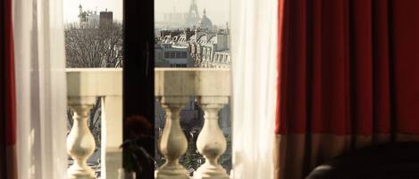 A hotel room with a balcony overlooking a cityscape, including a prominent tower.