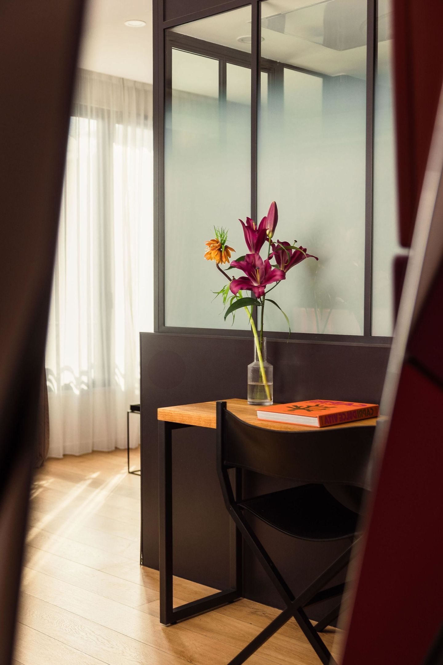 Una habitación moderna con una mesa de madera, una silla negra y un jarrón con flores.