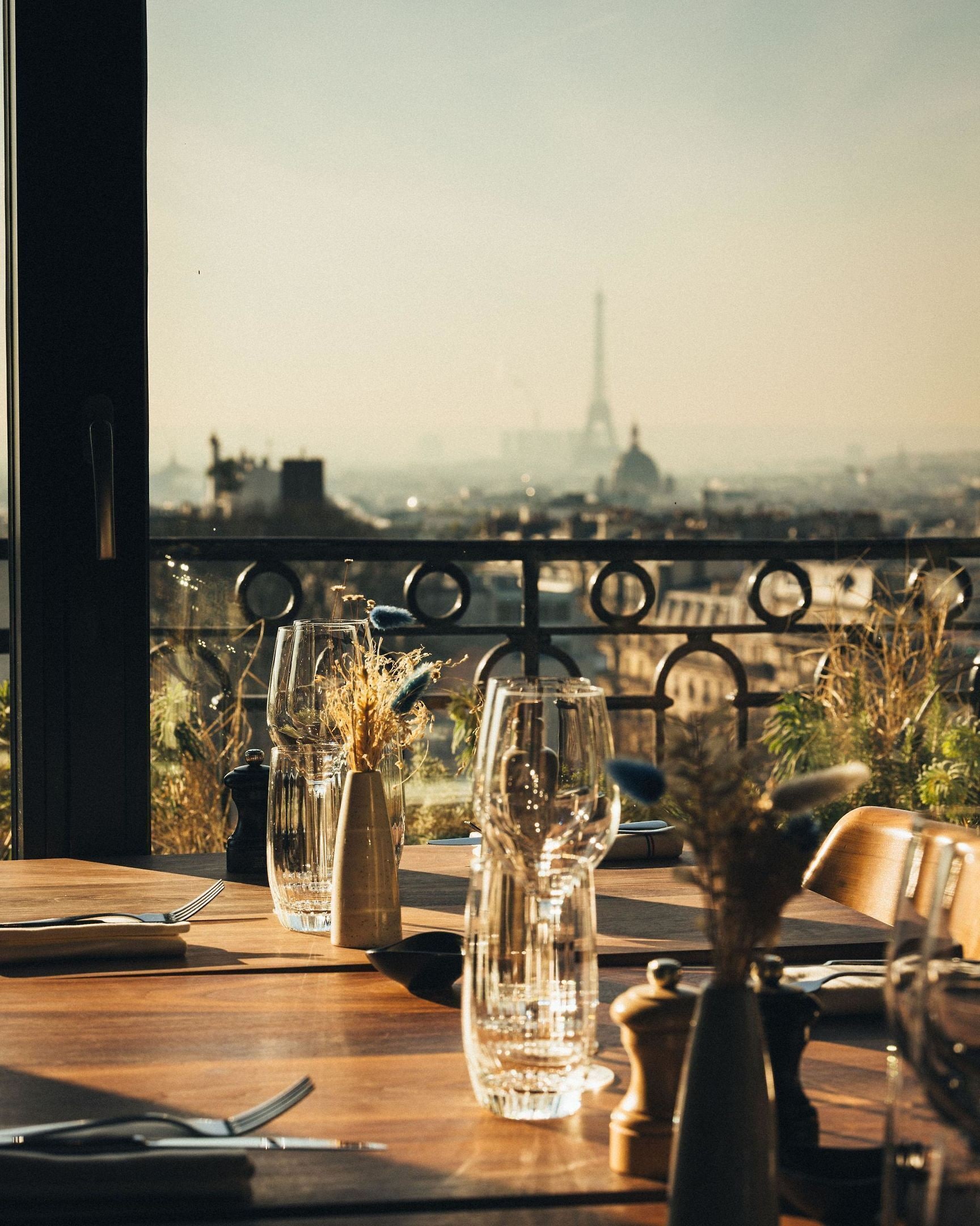 Een eettafel met uitzicht op de Eiffeltoren, een glazen vaas met gedroogde planten en een metalen hekwerk.