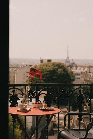 A balcony with a table set for a meal, a vase with dried flowers, and a view of the Eiffel Tower in the background.