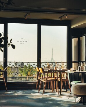 A dining area with a view of the Eiffel Tower, featuring a table set for two with chairs, a balcony railing, and potted plants. - Terrass'' Hotel (Paris)