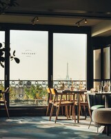 Un espace repas offrant une vue sur la Tour Eiffel, avec une table dressée pour deux personnes, des chaises, une balustrade de balcon et des plantes en pot.