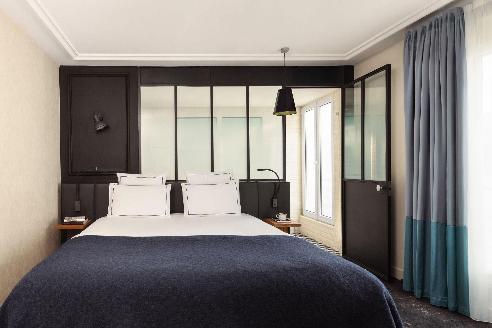 Una habitación de hotel moderna con una cama grande, una mesita de noche, una lámpara y vistas al exterior a través de una ventana.