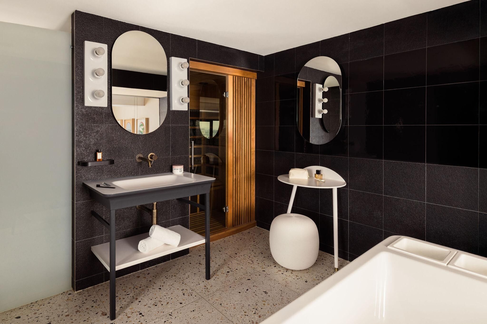 A modern bathroom with a vanity, two mirrors, a bathtub, and a wooden door.