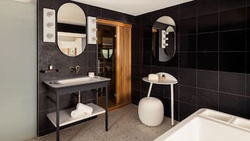 A modern bathroom with a vanity, two mirrors, a bathtub, and a wooden door.