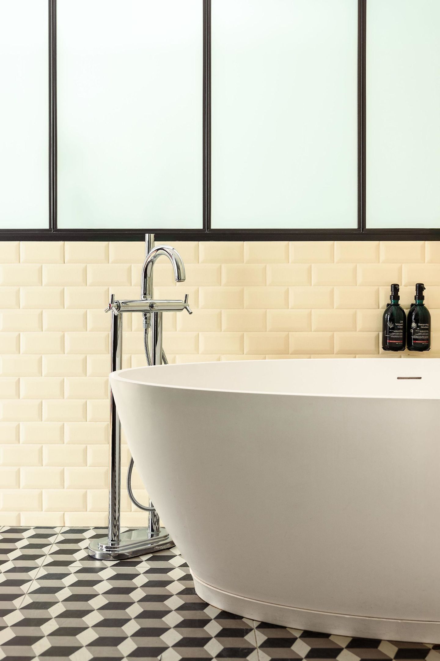 Ein modernes Badezimmer mit einer freistehenden Badewanne, einem Chrom-Wasserhahn und zwei Shampooflaschen an der Wand.
