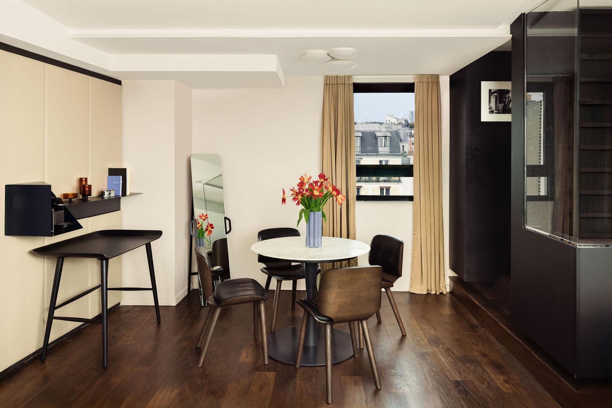 A modern hotel room with a dining area featuring a round table, chairs, and a vase of flowers.