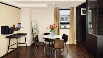 A modern hotel room with a dining area featuring a round table, chairs, and a vase of flowers.