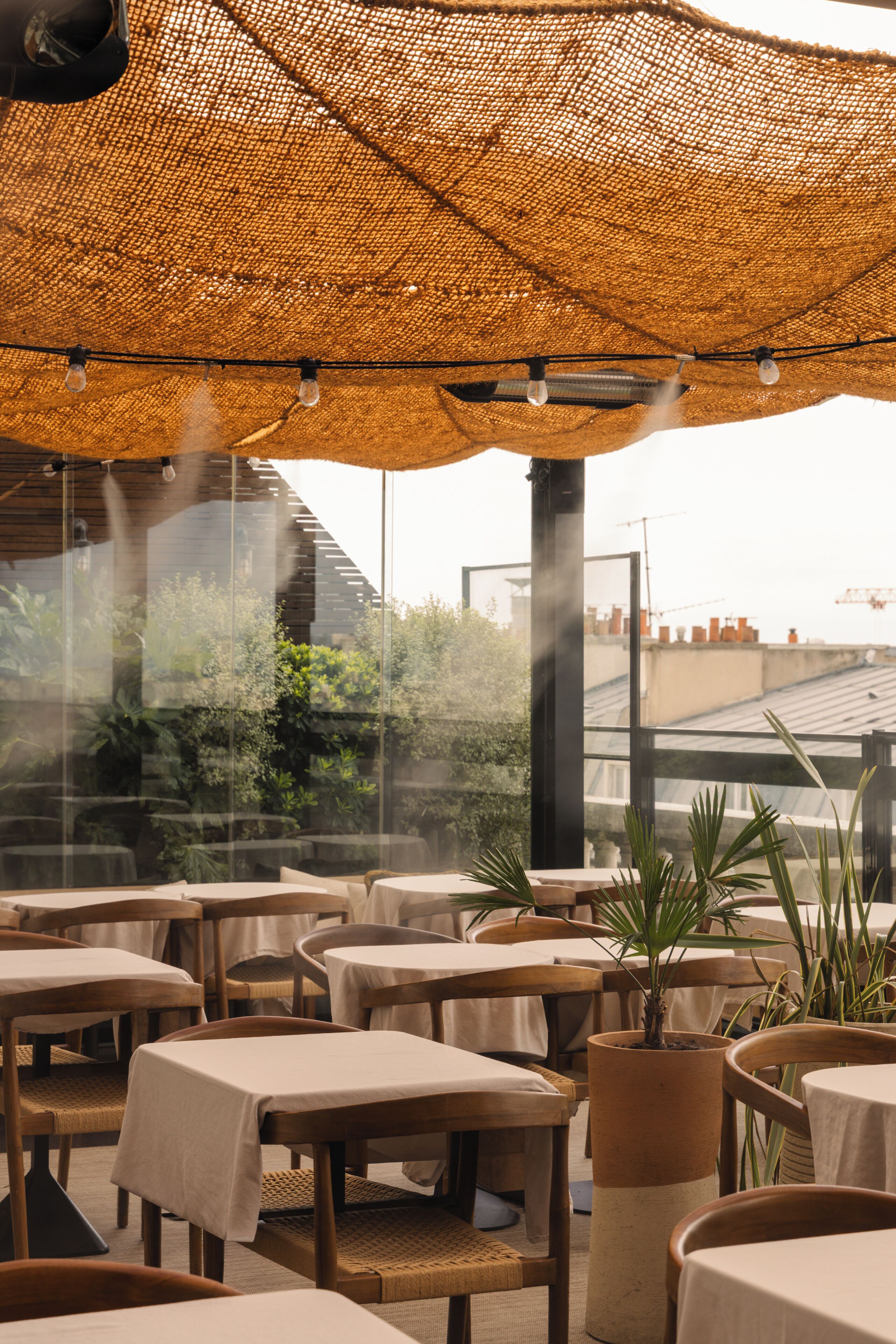 An outdoor dining area with tables and chairs, a large woven canopy, and potted plants.