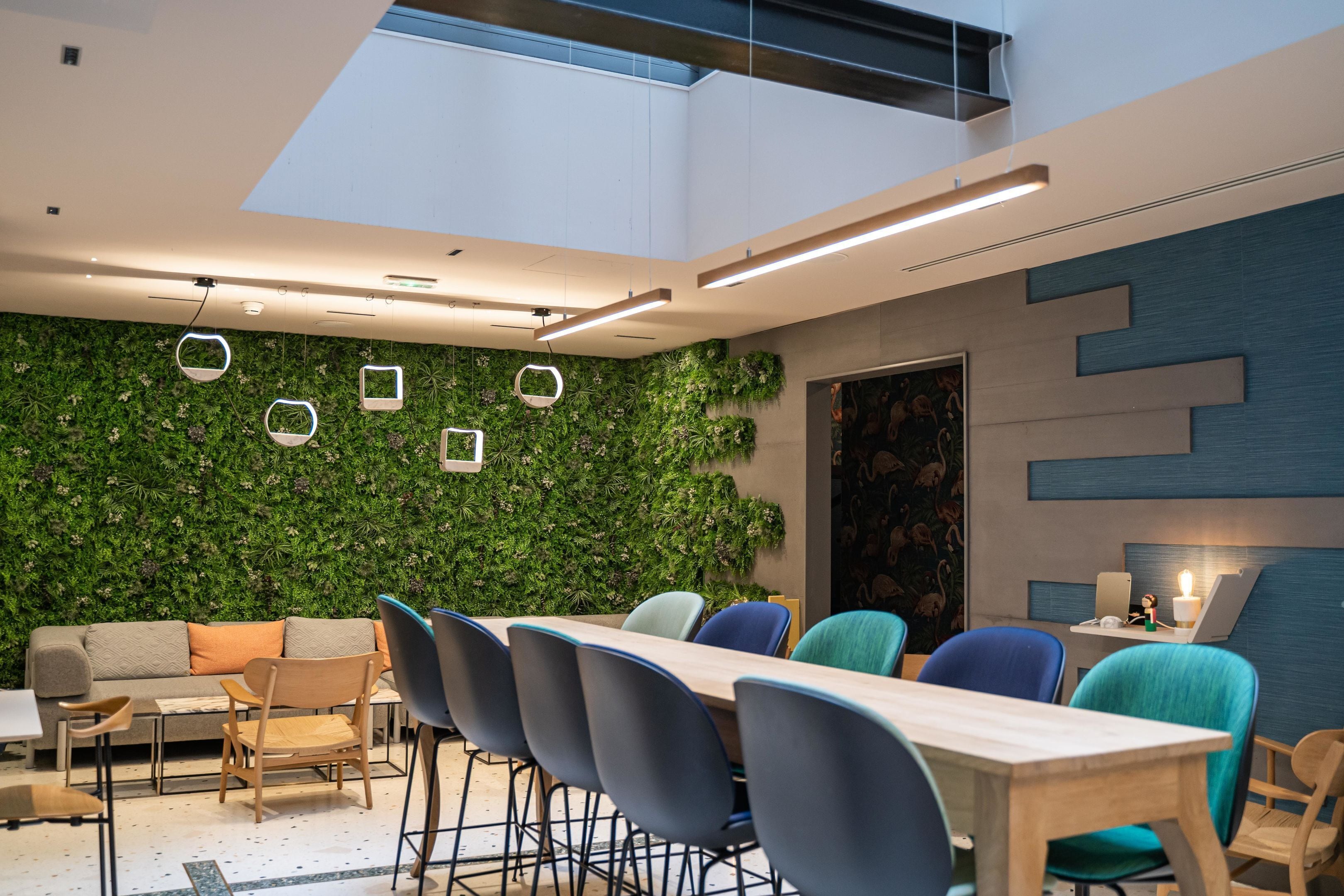 A modern meeting room with a green wall, wooden furniture, and a skylight.