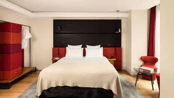 Ett modernt hotellrum med en stor säng, en röd garderob, ett litet bord med en bok och en röd fåtölj.