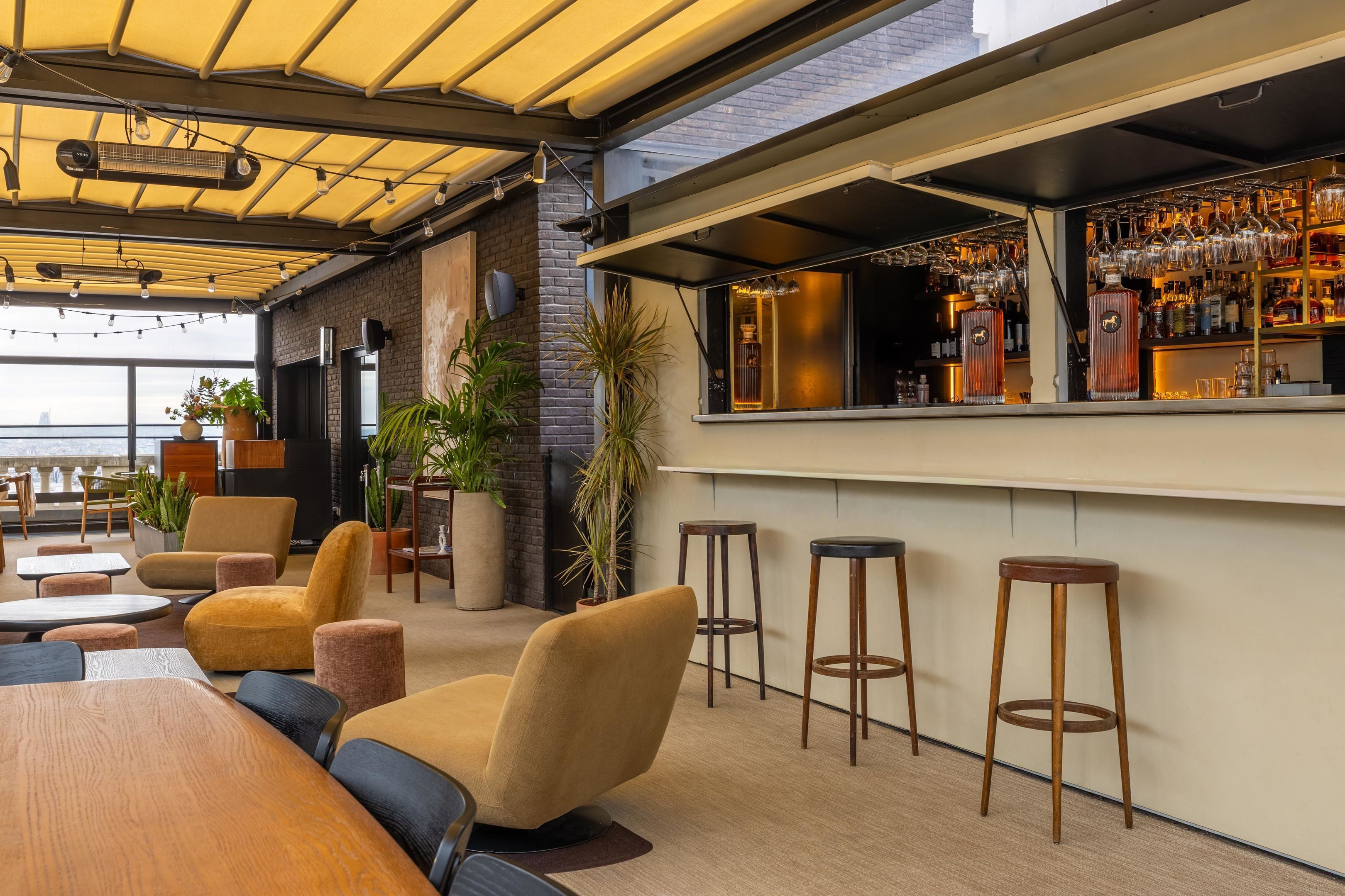 Zona de bar con taburetes, barra con botellas y vistas a la ciudad.