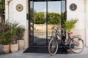 A bicycle parked in front of a building with a glass door, potted plants, and a sign with a key symbol.