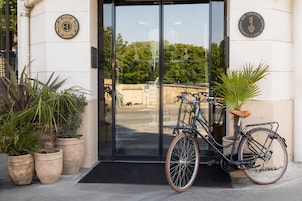 A bicycle parked in front of a building with a glass door, potted plants, and a sign with a key symbol.