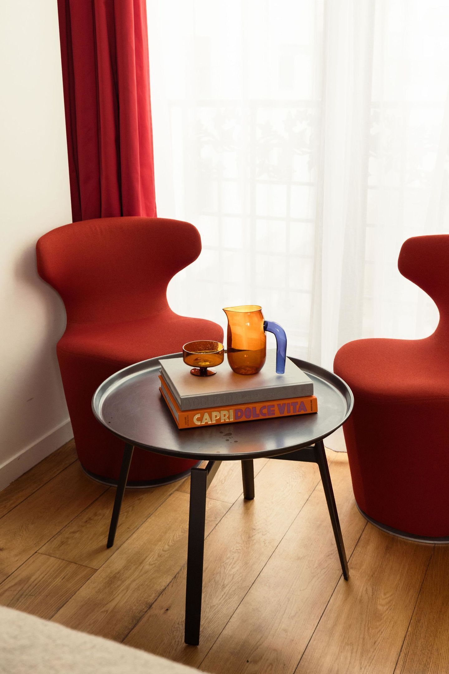 Una habitación con dos sillas rojas, una mesa redonda y un libro titulado "CAPRI DOLCE VITA" sobre la mesa.