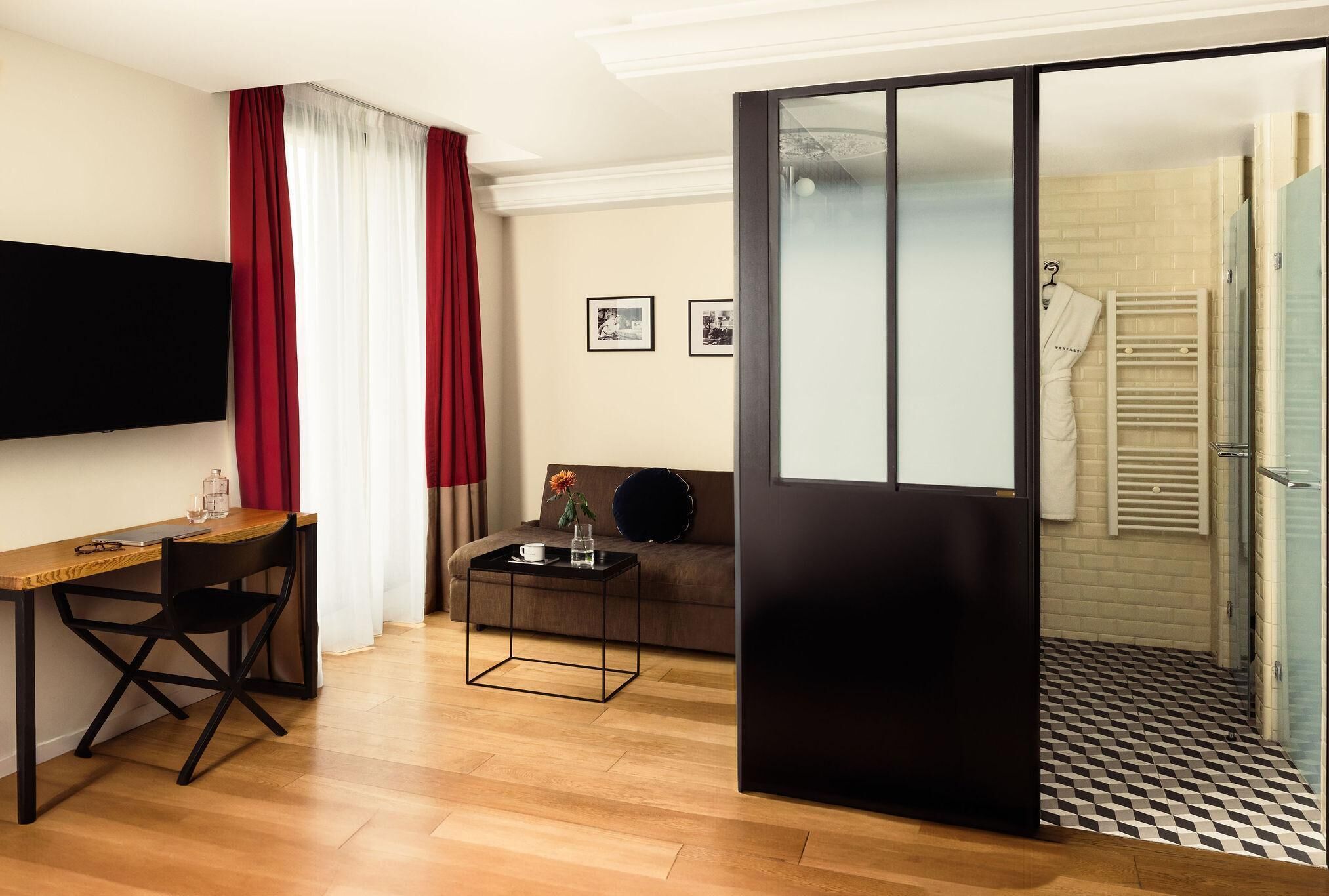 Una habitación de hotel moderna con un escritorio de madera, un sofá, un televisor y una puerta corredera que da al baño.