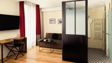 Una habitación de hotel moderna con un escritorio de madera, un sofá, un televisor y una puerta corredera que da al baño.