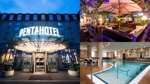 Exterior de un hotel al anochecer, con un cartel llamativo, un área de estar al aire libre con sombrillas y una piscina cubierta.