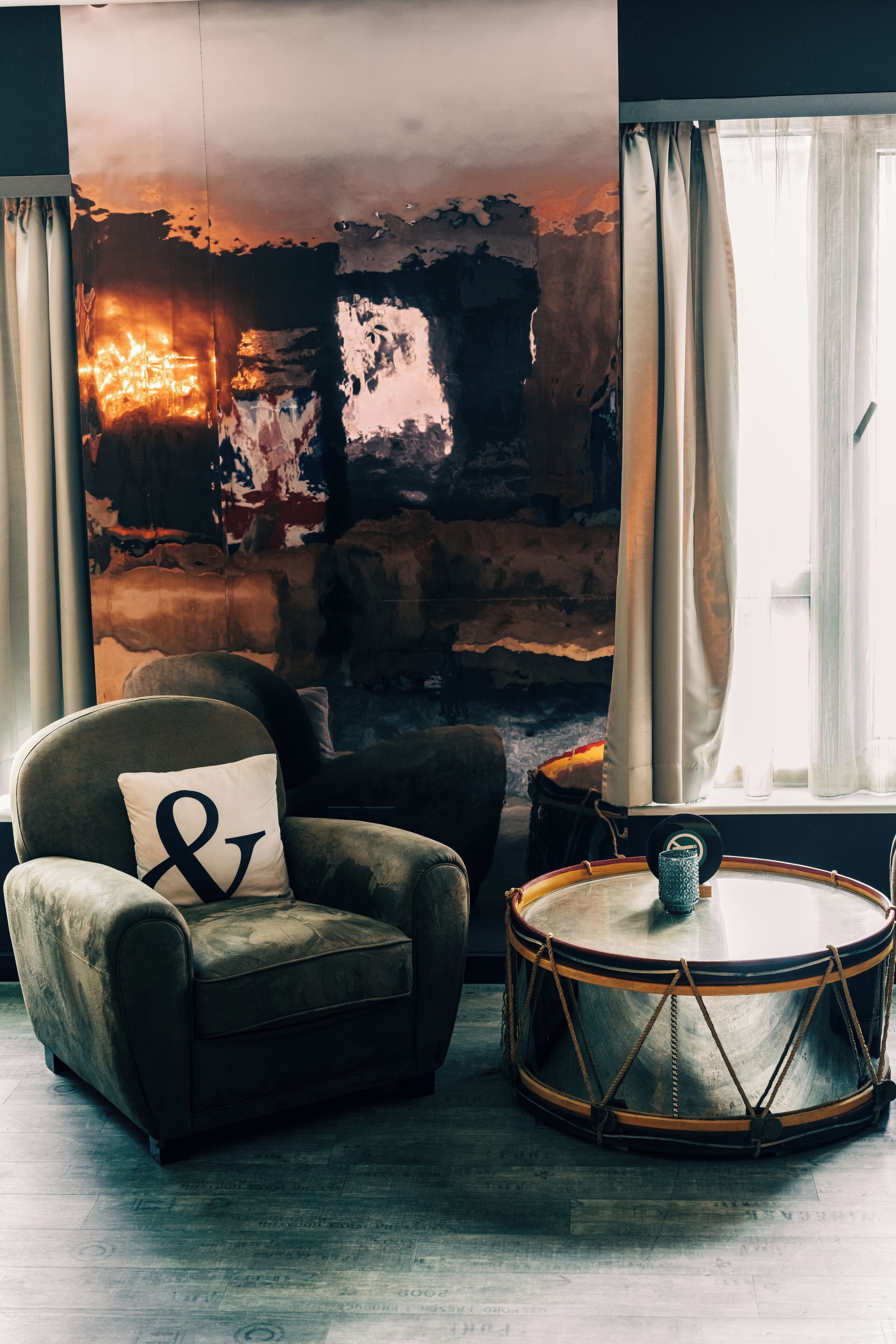 A room with a stone wall, a leather armchair with a pillow, a drum, and a window with curtains.