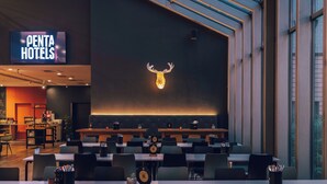 Un salón de conferencias con mesas y sillas, una pantalla grande mostrando 'PENTA HOTELS' y una escultura de cabeza de ciervo montada en la pared.