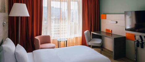Habitación de hotel con cama, escritorio, silla, televisión y ventana con cortinas.