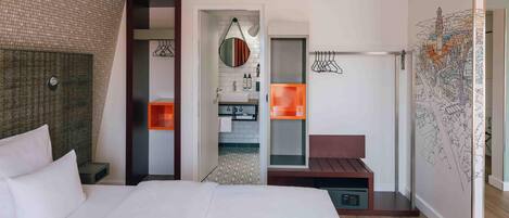 A hotel room with a large bed, a bathroom with a mirror, and a wall with a cityscape mural.