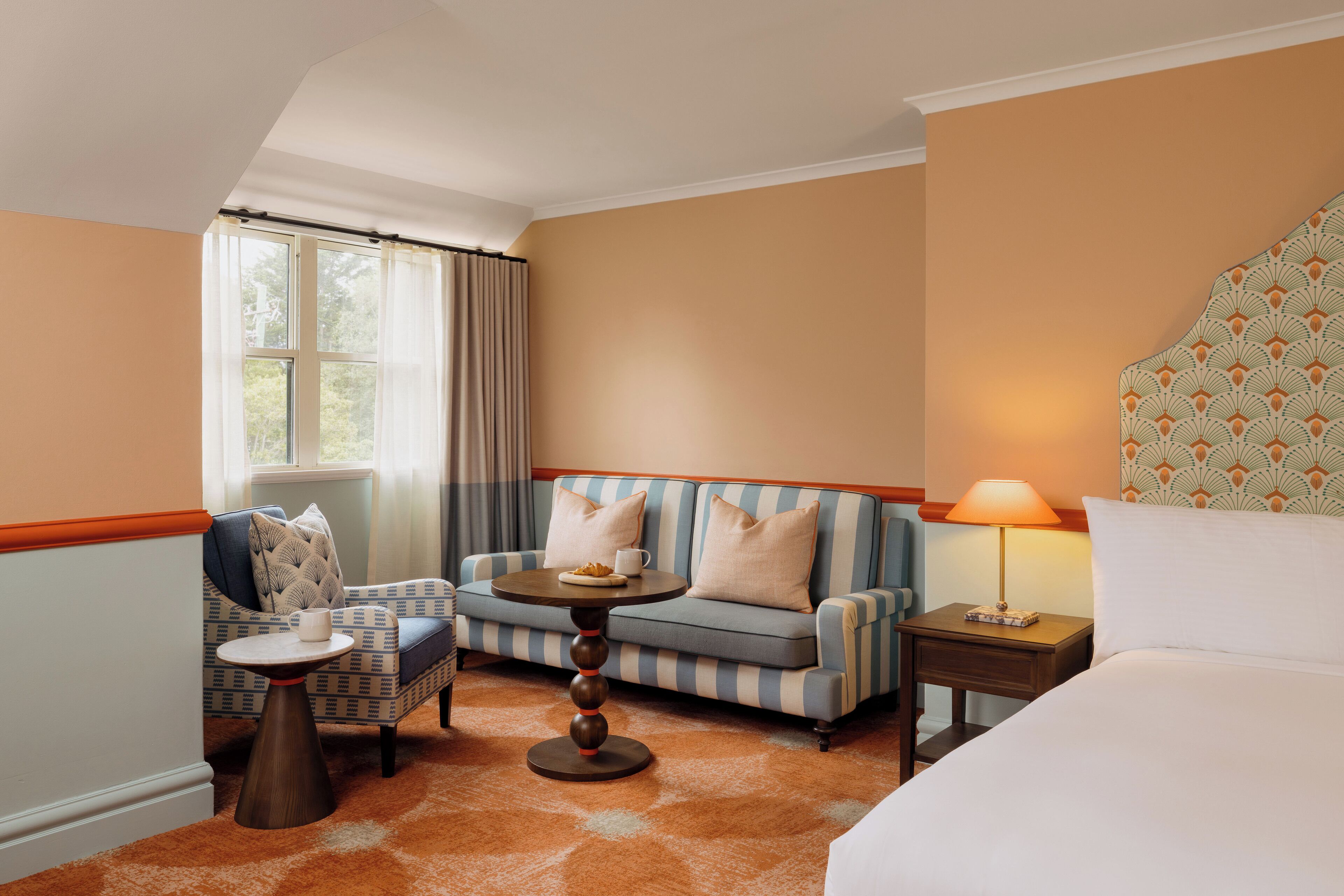 Habitación de hotel con sofá, sillón y una pequeña mesa con lámpara.