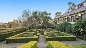 Un jardin à la française, avec des haies aux formes géométriques, un chemin central et un bâtiment doté de grandes fenêtres et d’un balcon.