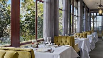 A restaurant with tables set for dining, large windows, and a view of trees.