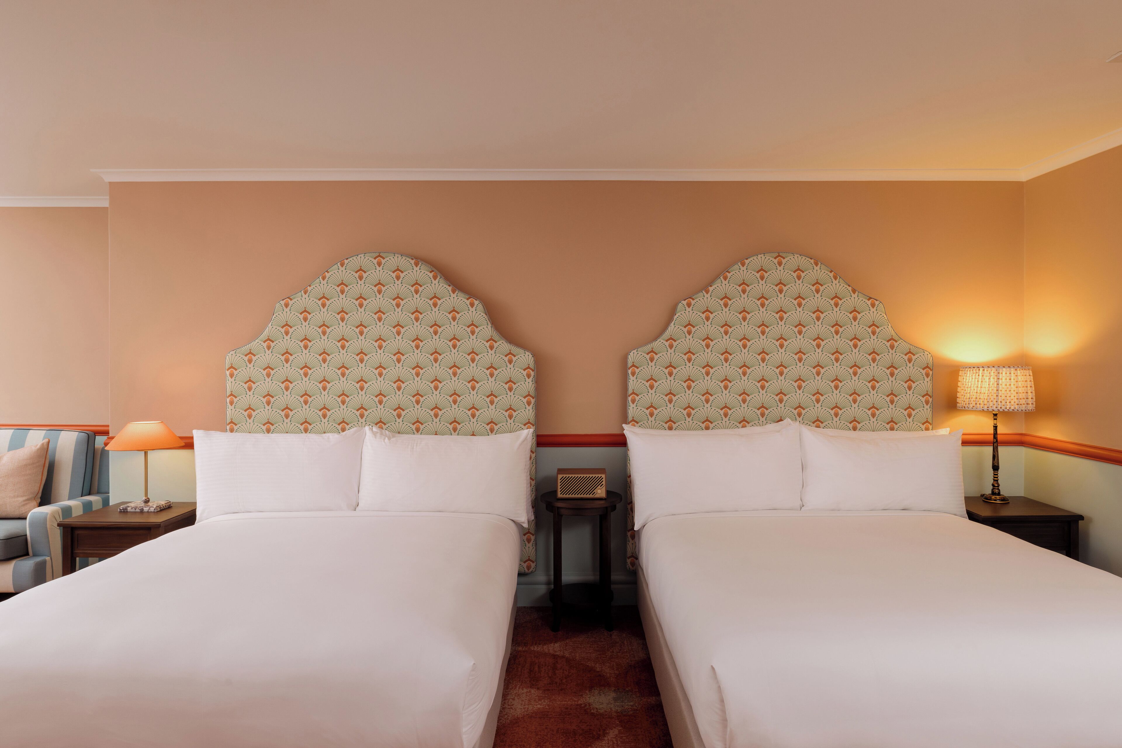 A hotel room with two beds, a sofa, a nightstand with a lamp, and a small table with a radio.