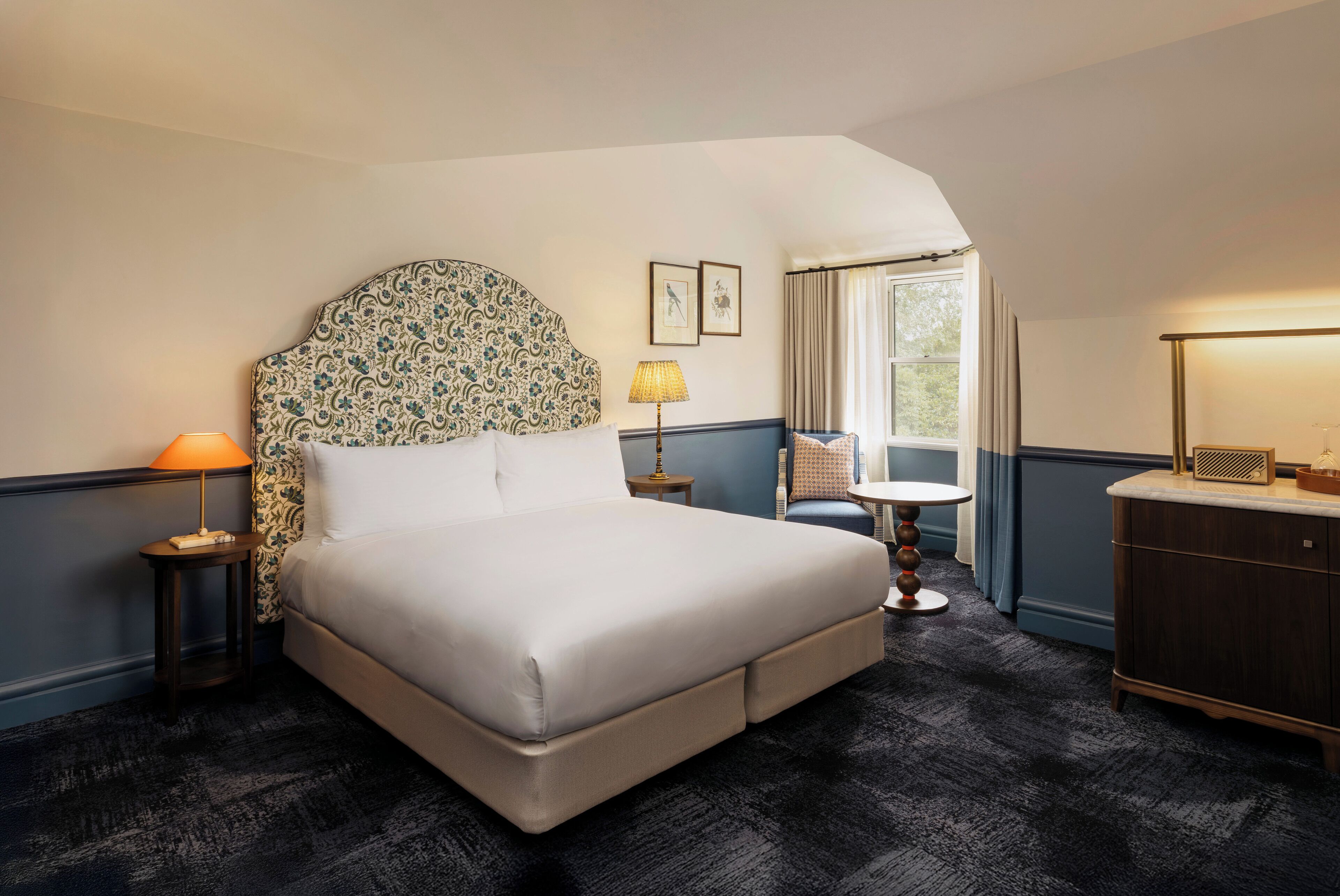 A hotel room with a large bed, a small table, a lamp, and a view of the outdoors.