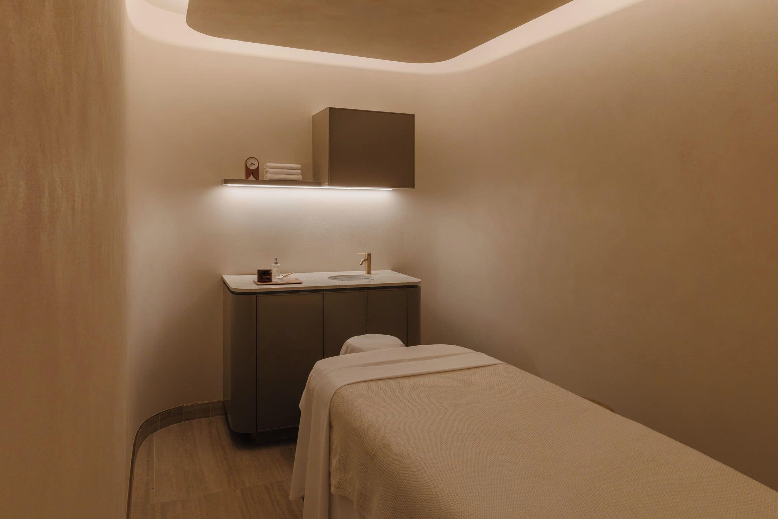 A small, dimly lit room with a single bed, a bedside table, and a built-in cabinet above the bed.