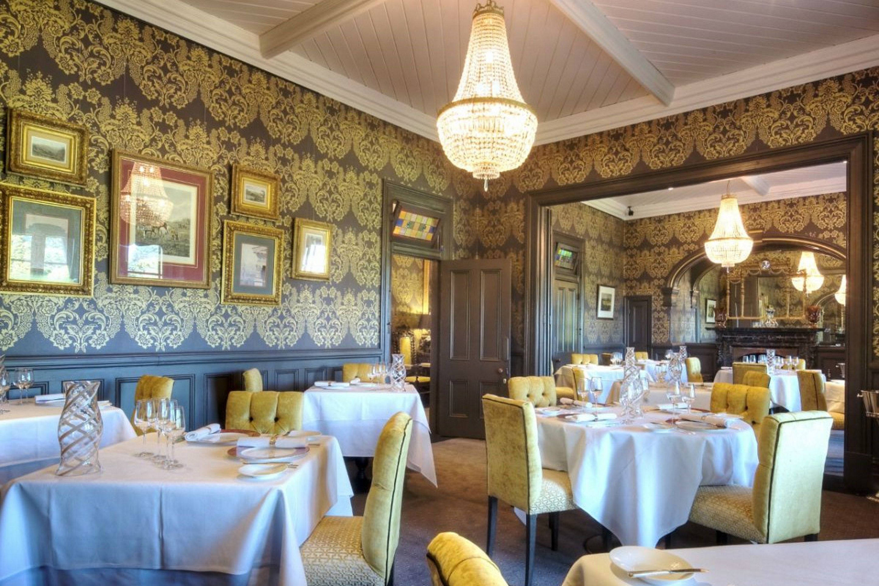 Ein Essbereich mit gedeckten Tischen, gerahmten Bildern an der Wand und einer Chandelier.