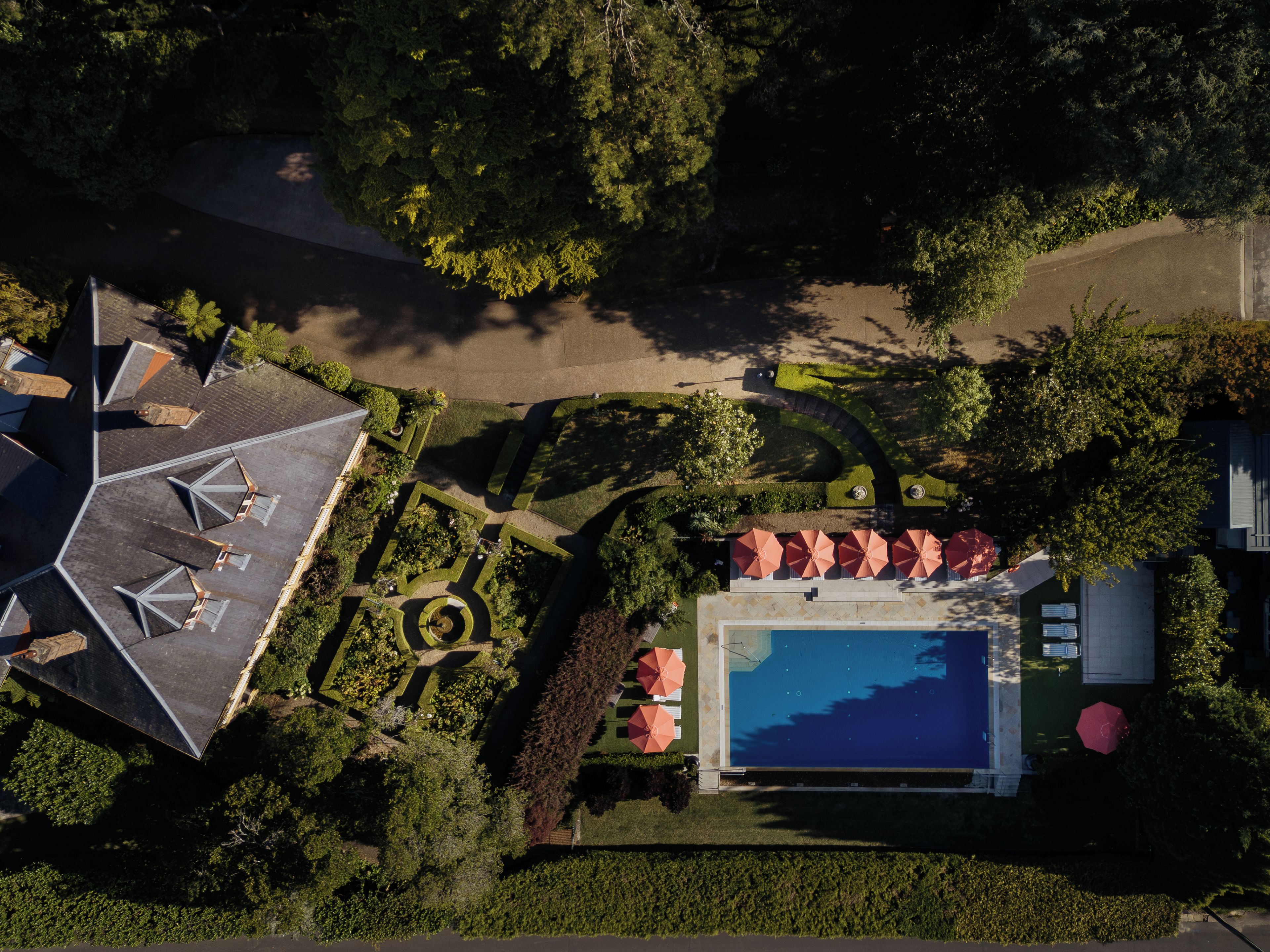 An aerial view of a resort with a swimming pool, sun loungers, and a well-maintained garden.